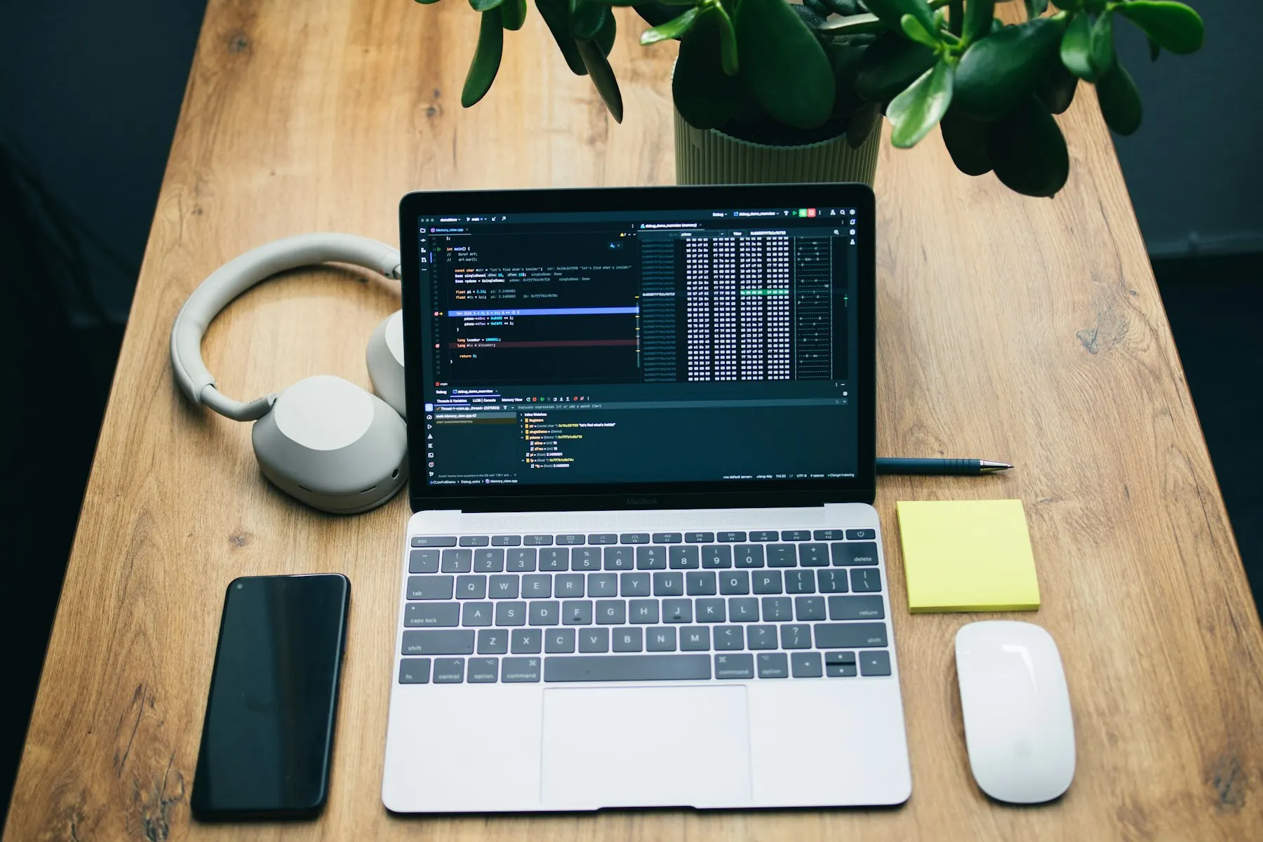 Laptop showing code on a wooden desk with headphones, phone and notebook
